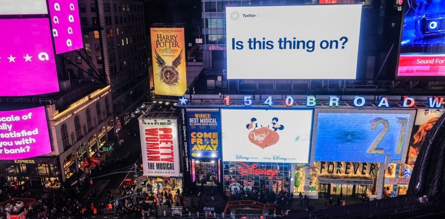 A busy New York City street with various billboards around. One looks like a giant Tweet with the words &quot;Is this thing on?&quot;