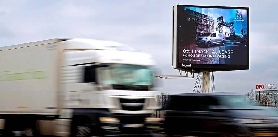 A busy highway with cars blurring by. On a billboard in the background is the Peugeot programmatic DOOH ad.