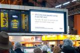 A photo of a large digital sign in London's Victoria Station. On the screen is the question &quot;who is the most beautiful woman in your life? why?&quot;