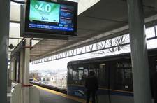 A digital display on a Vancouver SkyTrain platform. The display is showing news headlines, weather, advertising content, and a safety warning on different portions of the screen.