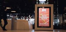 Two people walking by the XITE programmatic DOOH ad.