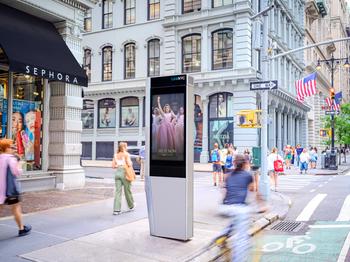 LinkNYC digital advertising kiosk on a busy New York City street corner, surrounded by pedestrians, cyclists, and storefronts.