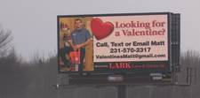 A somewhat grainy photo of a digital billboard that shows a man with a chainsaw standing in an equipment room. The ad asks &quot;Looking for a Valentine?&quot; and then offers contact information for people to get in touch with Matt.