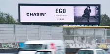 A digital billboard above a busy street. On the screen is an ad for EGO jeans.