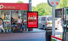 An exterior view of a gas station on the MMD network. A sign in the front, right next to the entrance to the store, displays an ad for Coca Cola.