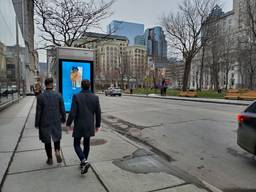 Two people walk by a Campsite digital out-of-home screen