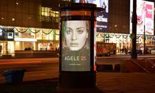 A digital poster in Warsaw, Poland. It is on the side of the street at nighttime, and displays an ad for the Adele album &quot;25.&quot;